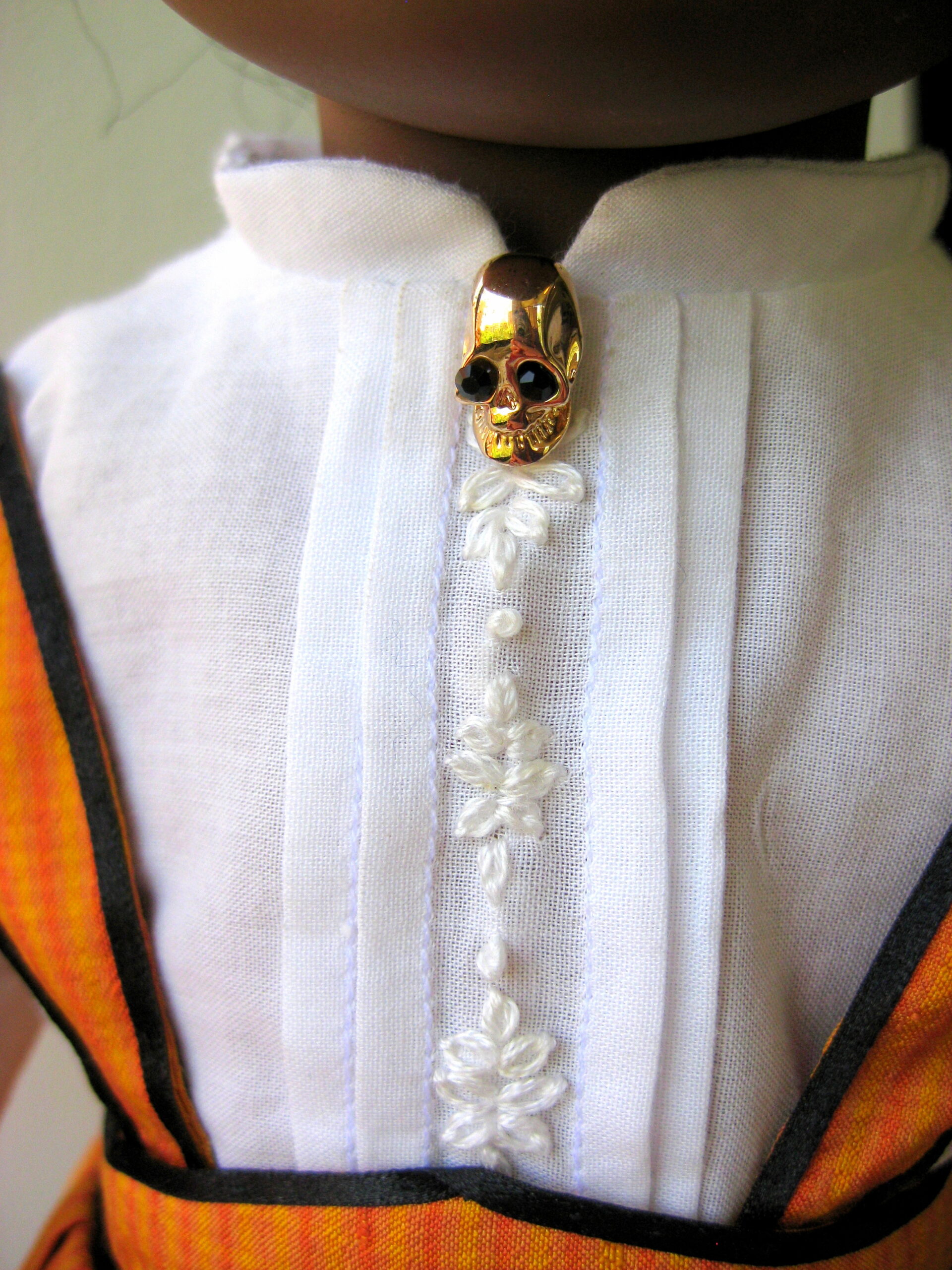 Close-up of an american girl doll blouse with pleating, embroidery, and a skull brooch at the neck