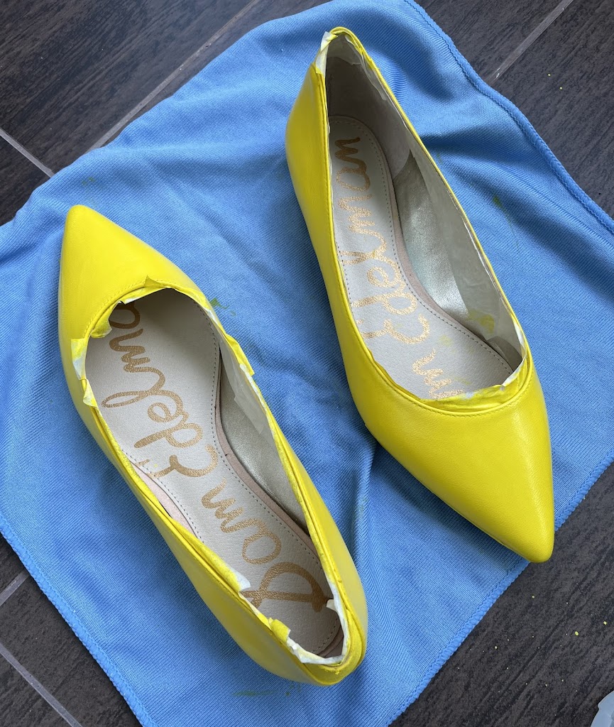 A pair of yellow painted 1790s shoes drying on a blue towel.