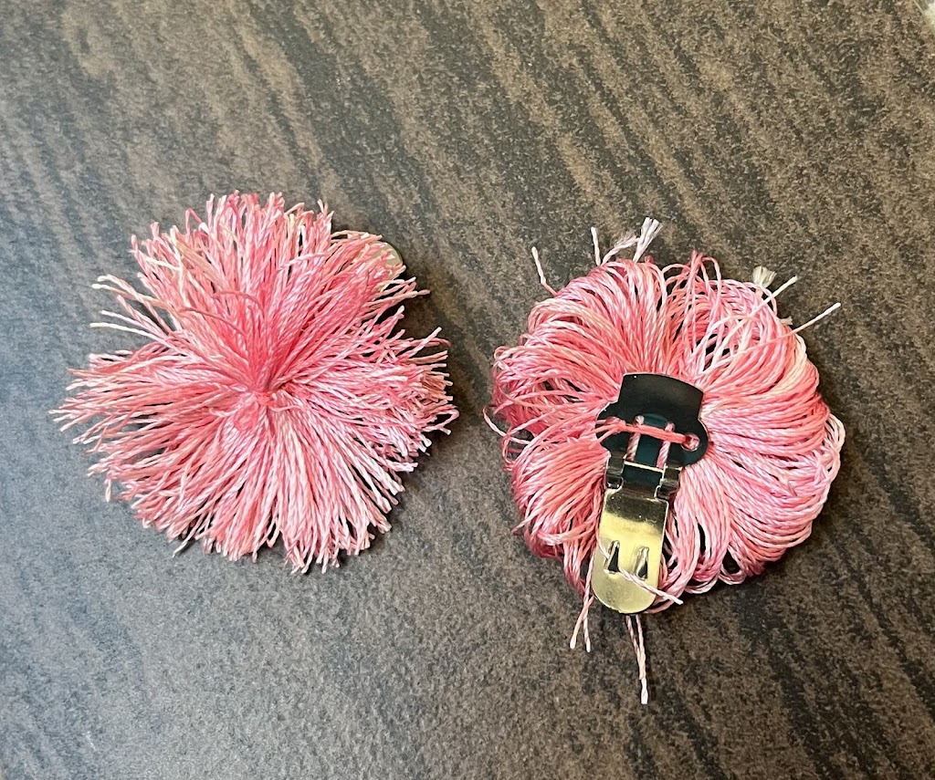 A pair of pompoms made of silk floss, one face up, one face down