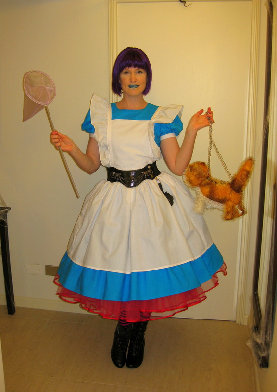 Alice of Wonderland faces the camera. She is holding a butterfly net and a purse made of cat stuffie toy.
