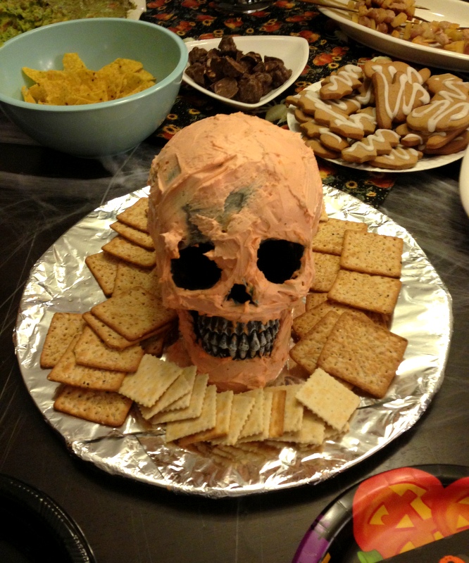 A fake Human skull sits on a plate. The skull is covered in dip and surrounded by chips