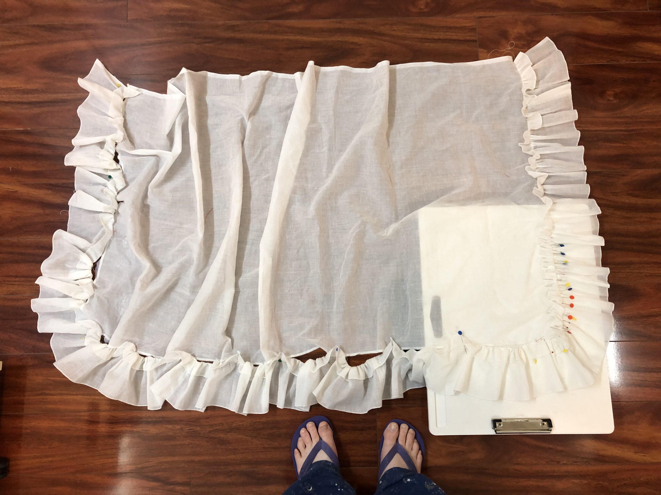 An apron laid out on the floor. The ruffle has been gathered and partially pinned to the edges of the apron.