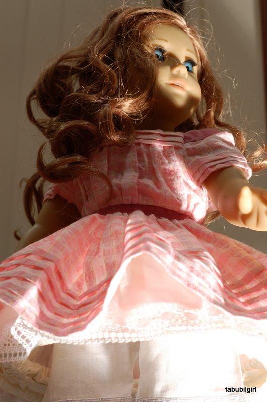 An american girl doll in a pink dress is lit and photographed from below. The effect is menacing.