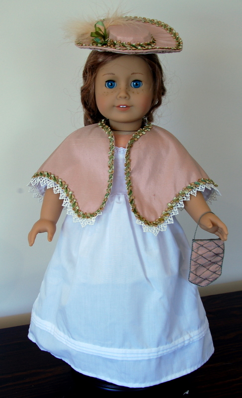 an american girl doll wears a late victorian ensemble consisting of a peach capelet, hat and purse
