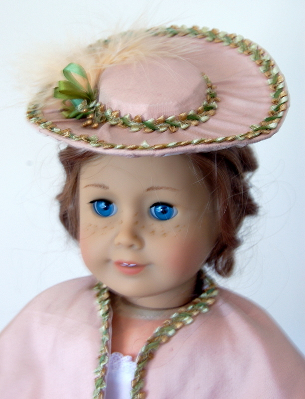 close up of an american girl doll wearing a victorian ensemble of capelet and hat