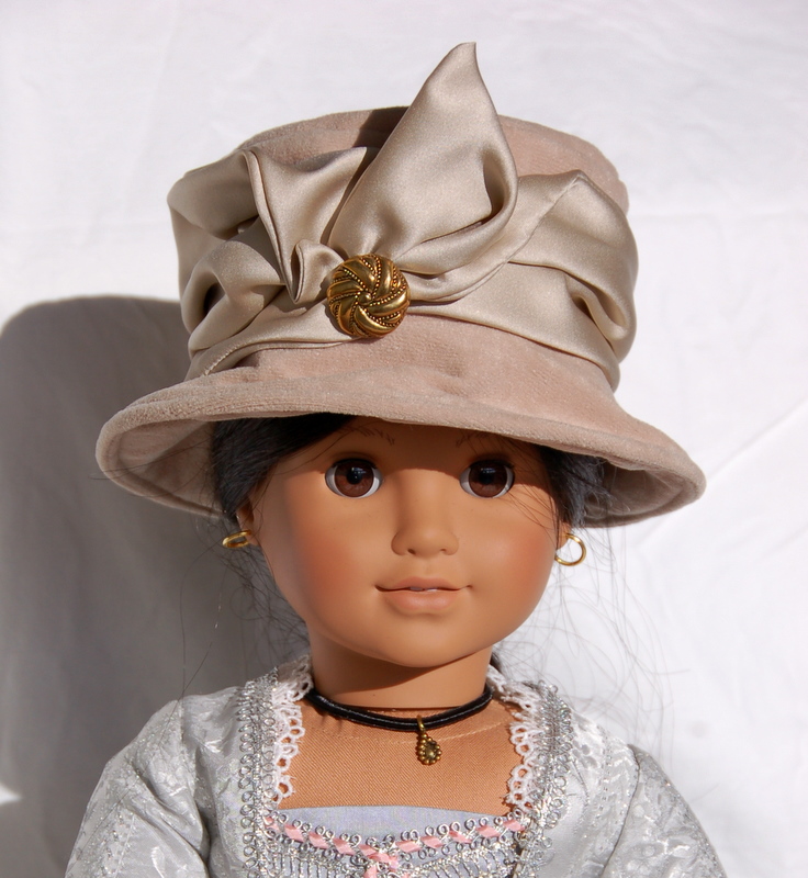 An american girl doll faces the camera wears a brown cloche hat with exuberant satin ribbon trim