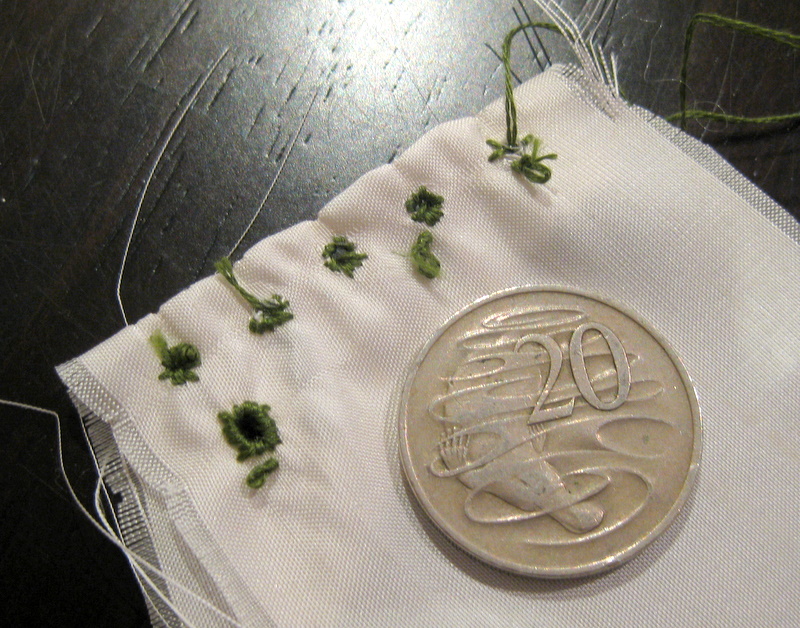 A set of practice doll-scale eyelets on a scrap of white silk.  They are very messy.