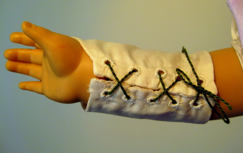 A doll arm wearing a white silk gauntlet with big green lacing