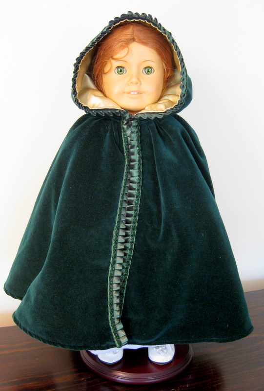 An American Girl Doll wearing a long green cloak with a hood