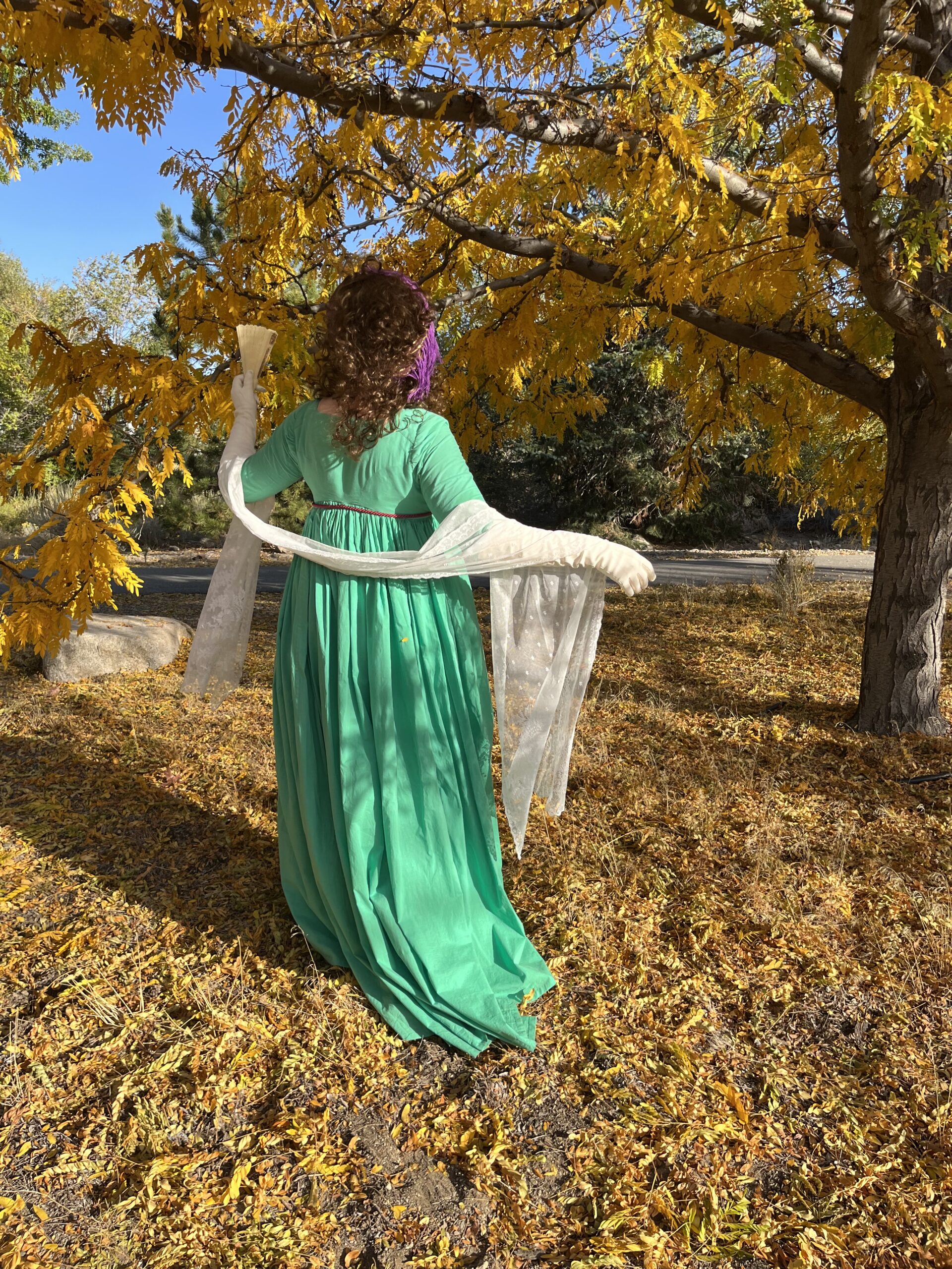 Tabubilgirl stands with her back to the camera, showing the back of her green 1790s round gown.