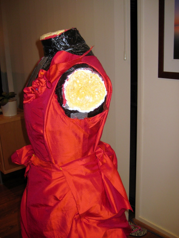 a red silk bodice is mounted on a mannequin. it is very wrinkled.