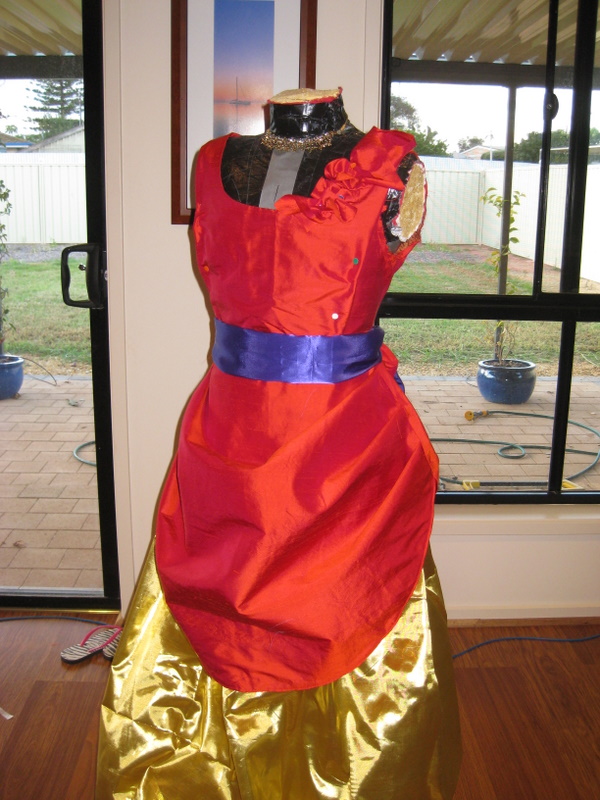 A fire red ballgown with a gold lame skirt and a purple sash are mounted on a mannequin