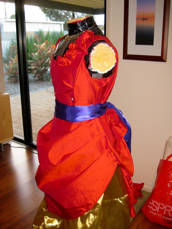 A red silk ballgown with a purple sash is mounted on a mannequin