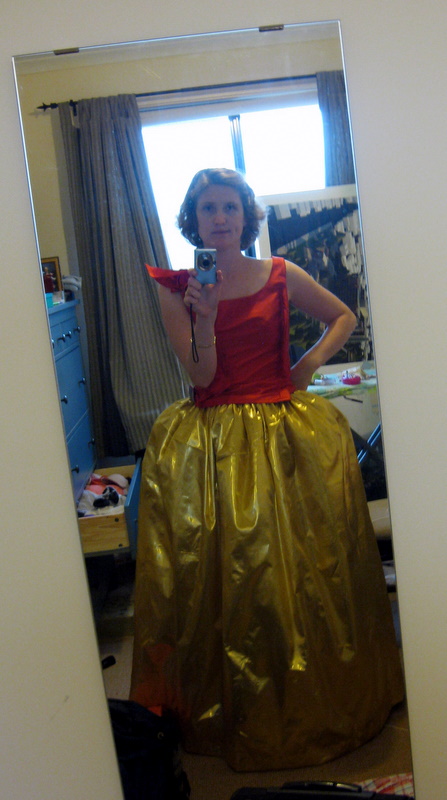 Tabubilgirl looks at a mirror. She is wearing a red silk bodice and an extremely large gold skirt