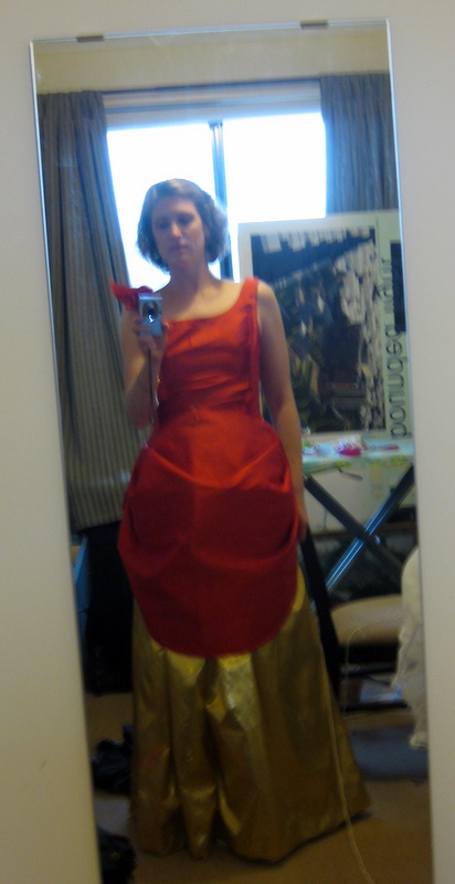 Tabubilgirl slouches in front of a mirror. She is wearing a fire red ballgown with an apron skirt