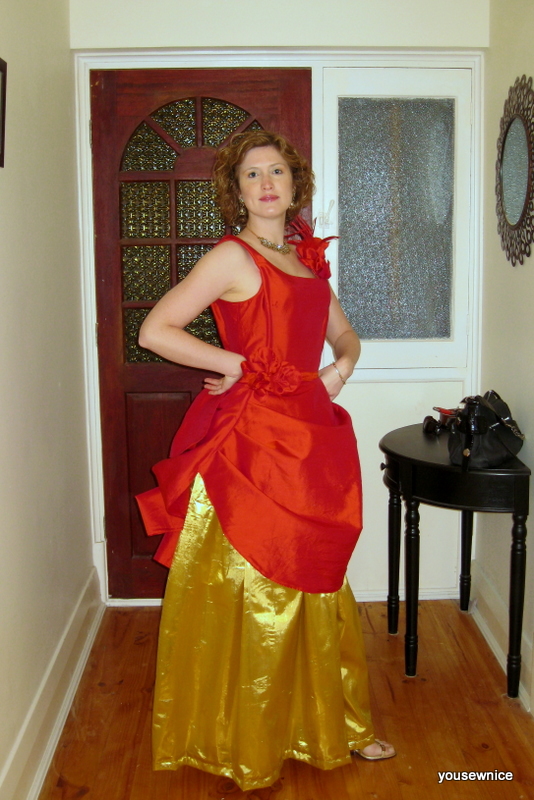 Tabubilgirl poses in a hallway, wearing a red silk gown draped over a gold lame underskirt.