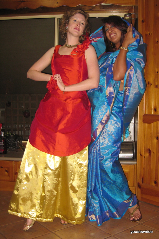 Two women pose - one wears a fire red and gold ballgown. the other wears an ice blue silk saree.