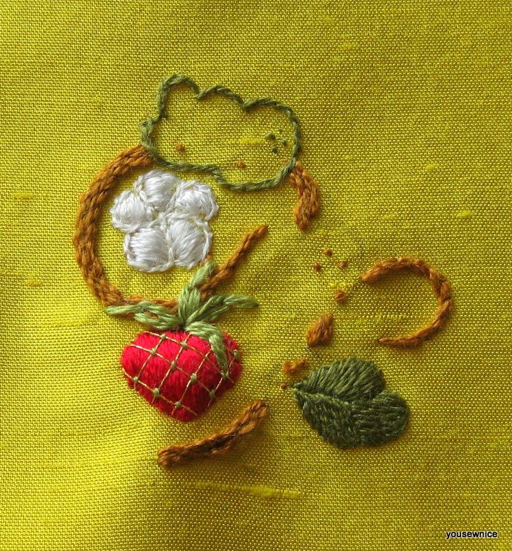 A half-finished pad-stitched embroidery piece showing a strawberry and strawberry flower.