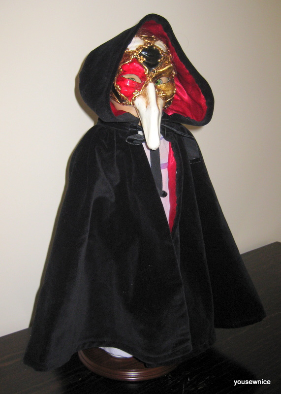 An American Girl doll is swaddled in a black velvet domino cloak and Venetian Doctor Mask