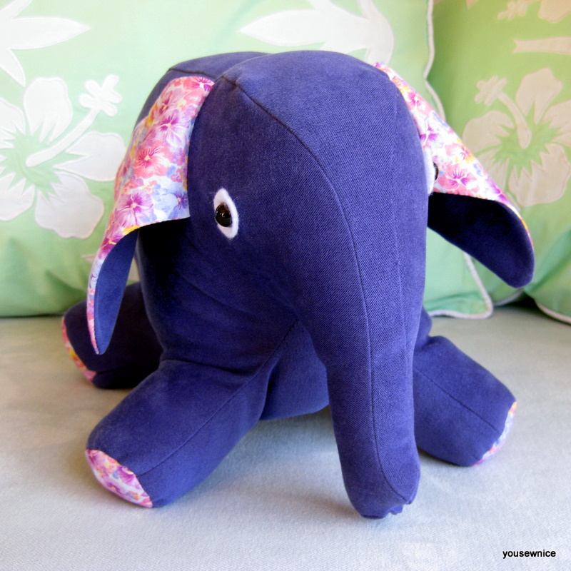 A stuffed purple elephant with pink feet and ears looks at the camera.