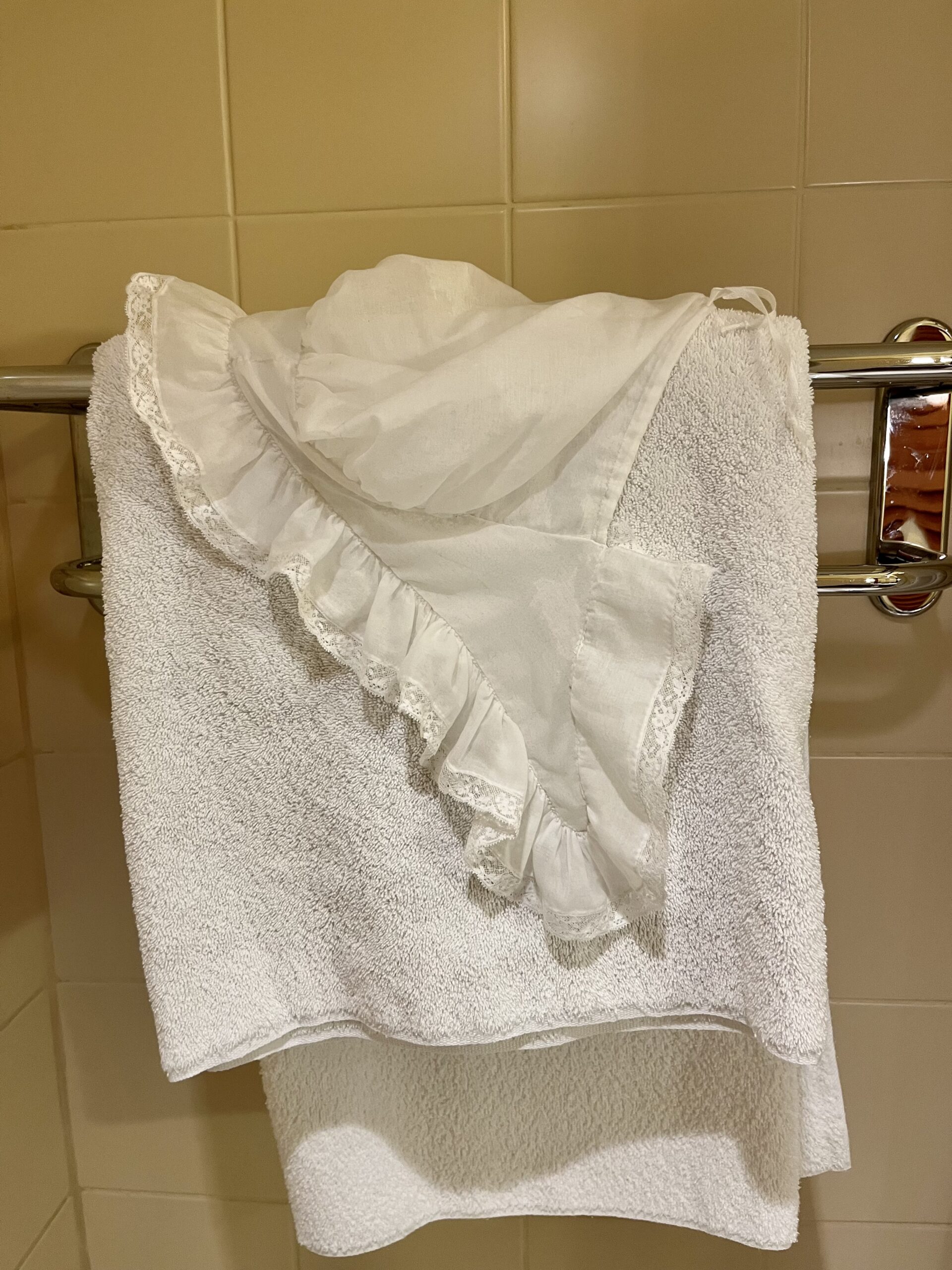 A lace-edged lappet cap hangs over a towel trail i a bathroom.