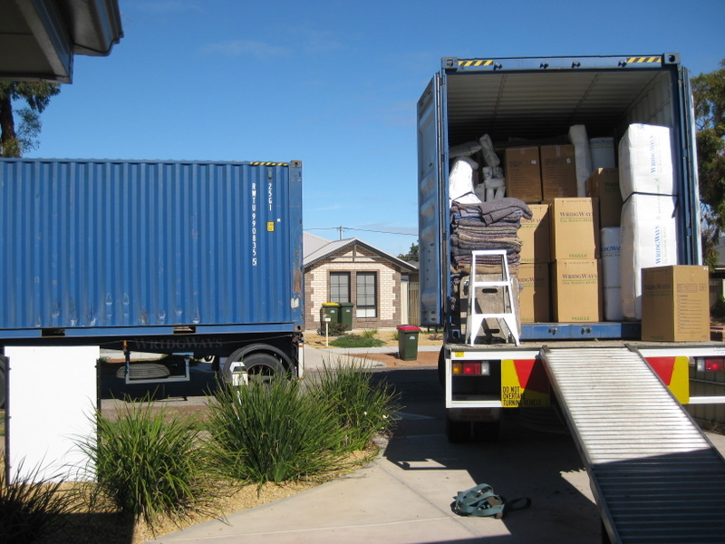 A moving truck stands open in front of a house. A ramp is let down from the moving truck.