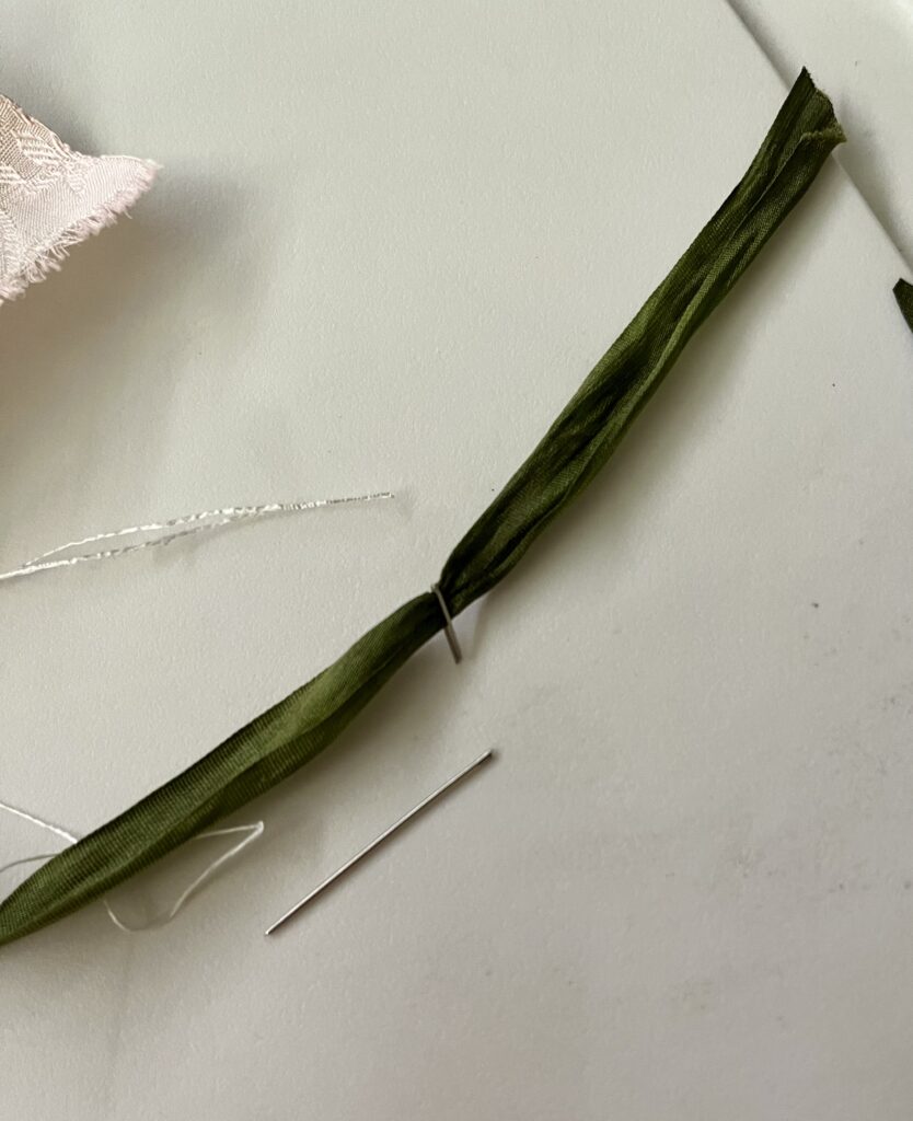 a snapped needle lies next to a green silk ribbon