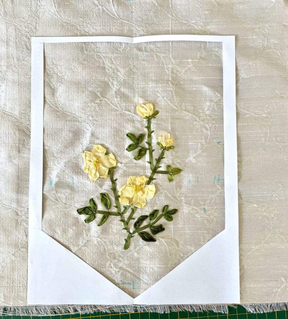 a paper template sits over a piece of silk embroidery