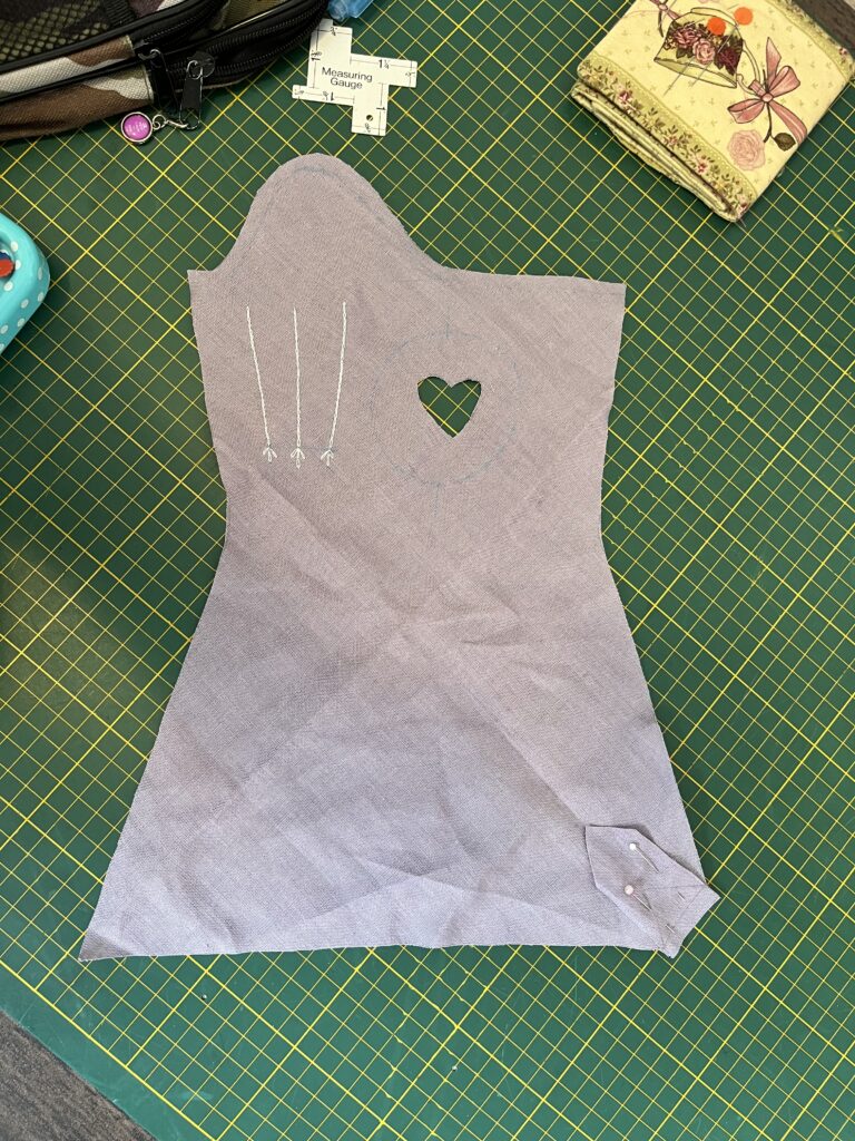 A lavender cut-out of a mitt lies on a green cutting board. The bottom right corner of the mitt has a small scrap of fabric pinned onto it.