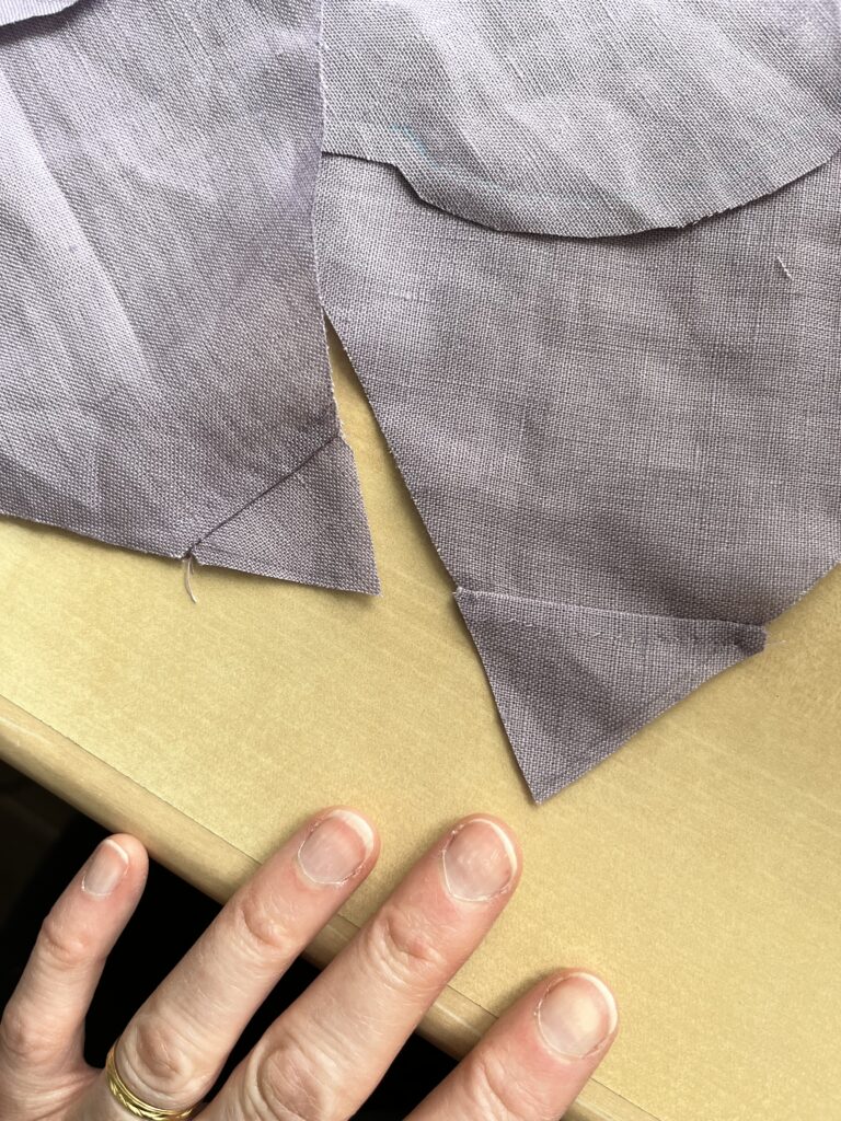 A hand points towards a piece of lavender linen with a corner stitched and felled.