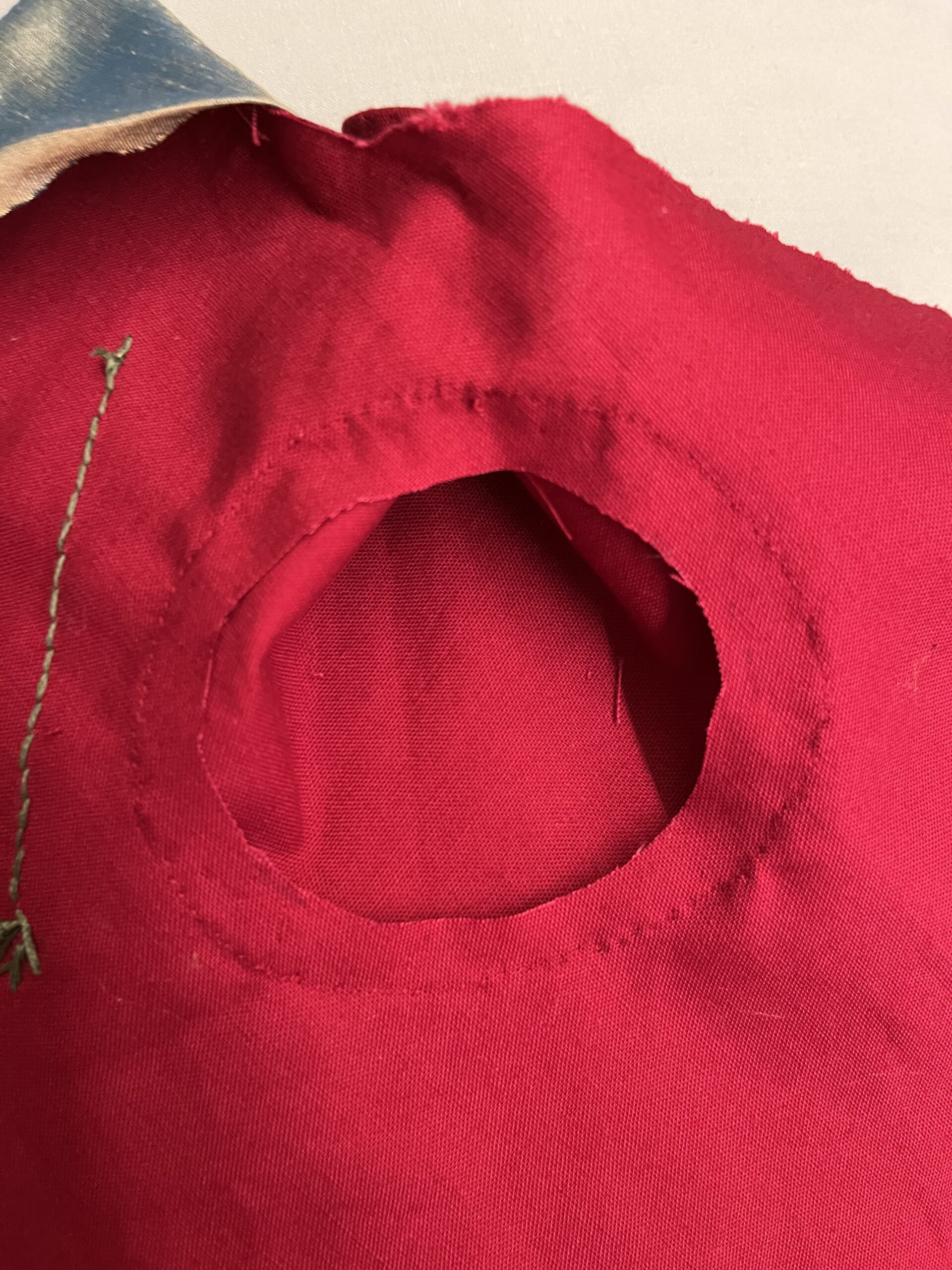 The inside of the thumb hole of a red 18th century mitt with the stitching line showing.