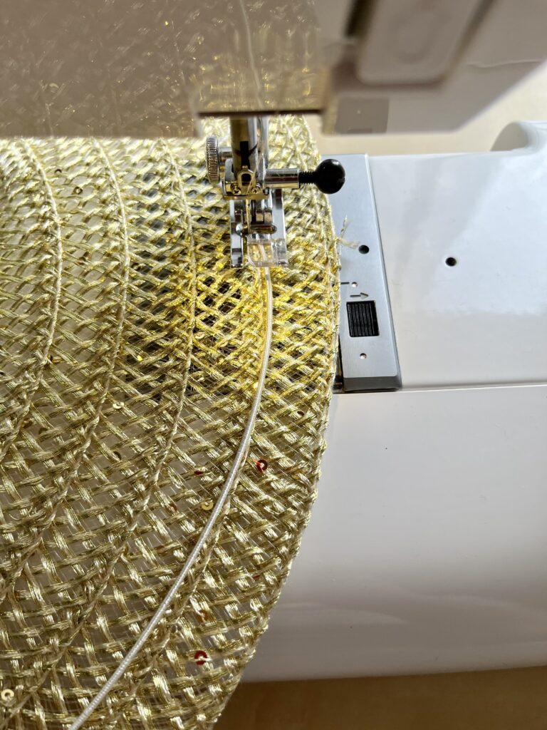 A sewing machine runs a zig szag stitch over a wire running along the edge of a gold place mat