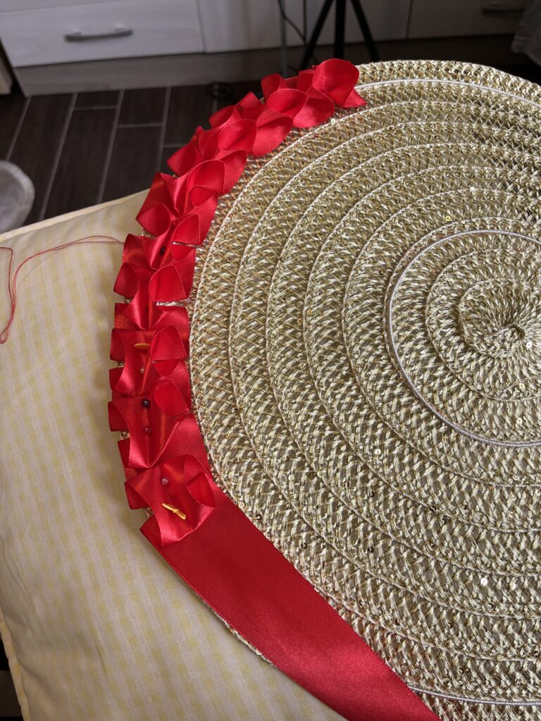 A row of box pleated red ribbon is being sewn onto the edge of a gold placemat