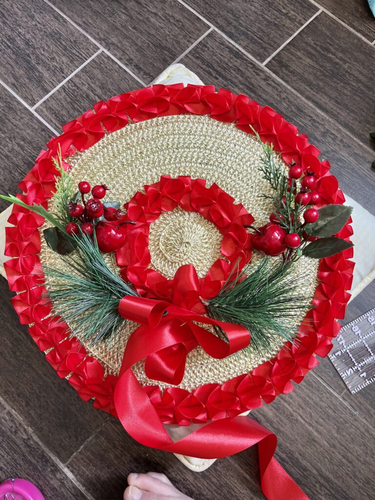 An 18th Century Bergere Hat is trimmed for christmas, with box pleated red ribbon and christmas berries and evergreen needles