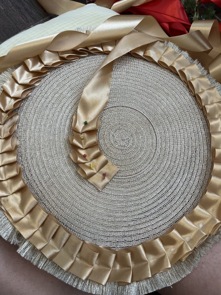 A gold placemat is being trimmed with two rows of knife-pleated gold ribbon - one row along the edge and one row around the center