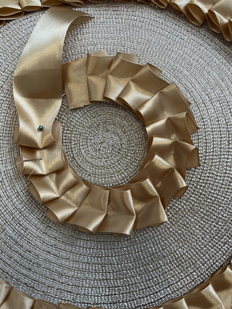 Gold ribbon being box pleated in a circle around the center of a gold placemat