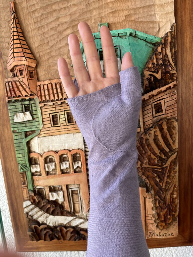 A hand wearing a purple linen 18th Century mitt faces the camera palm-up