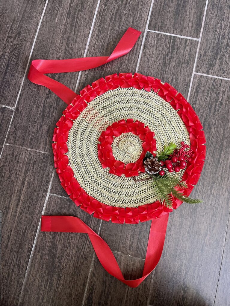 An 18th Century Bergere Hat lies on the floor - it is trimmed for christmas, with box pleated red ribbon and christmas berries and evergreen needles