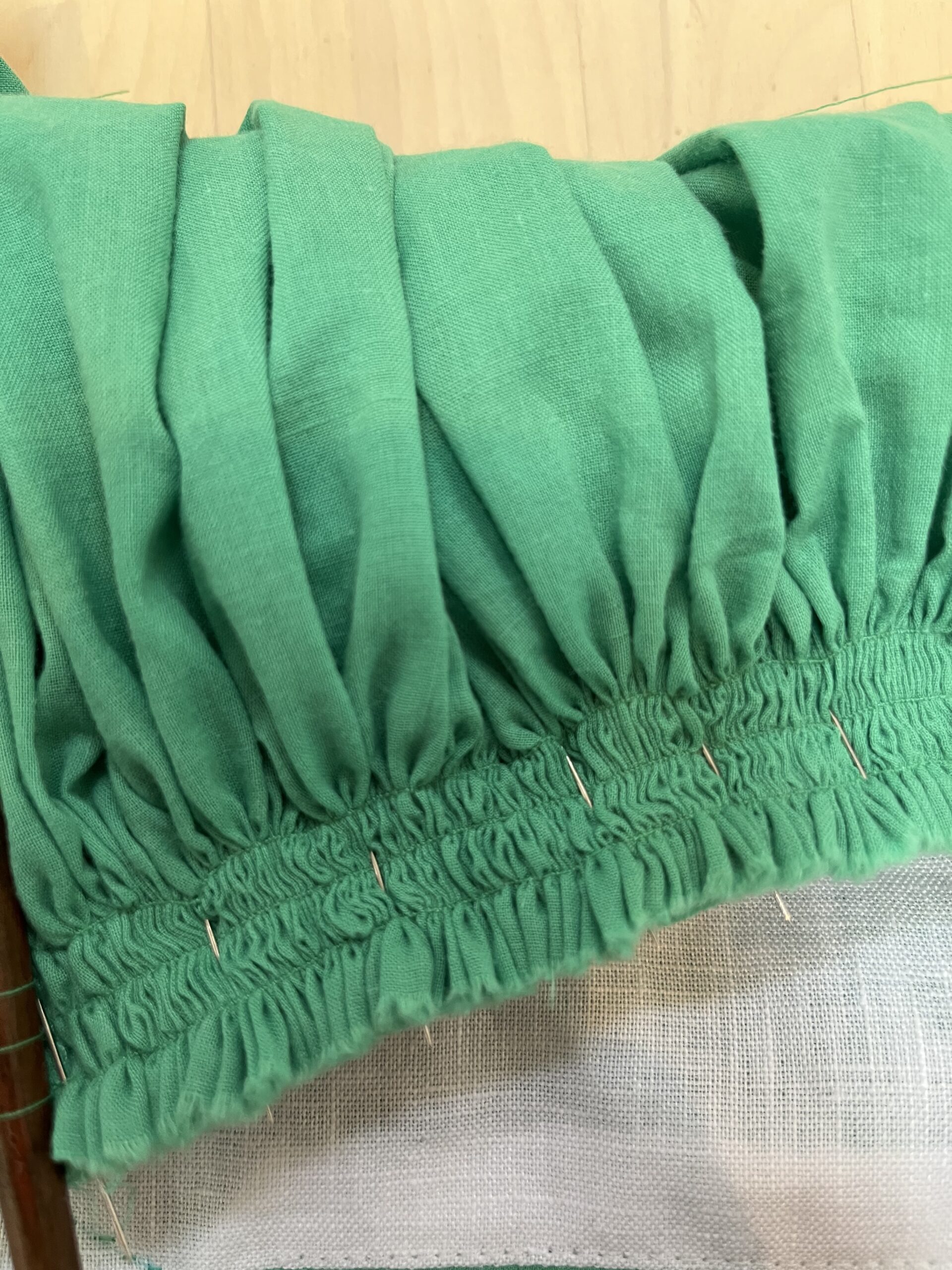A close-up view of three rows of gathering on green cotton voile.