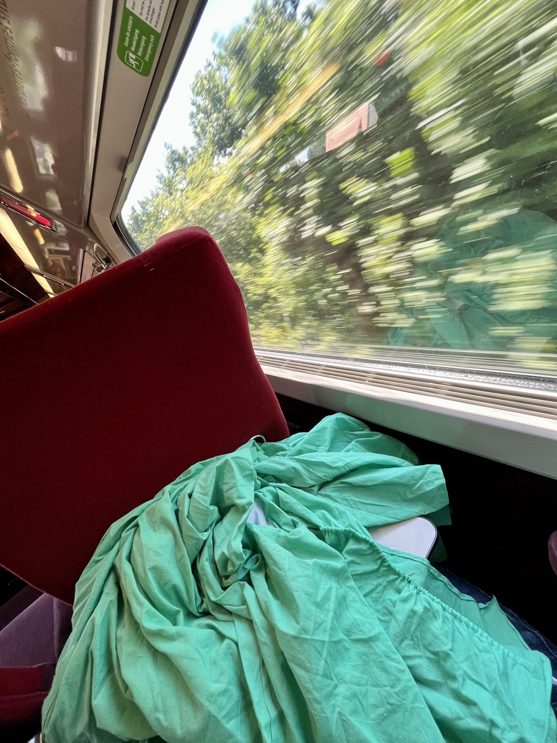 A green dress sits on the fold-down table on the back of a the seat on a moving train.