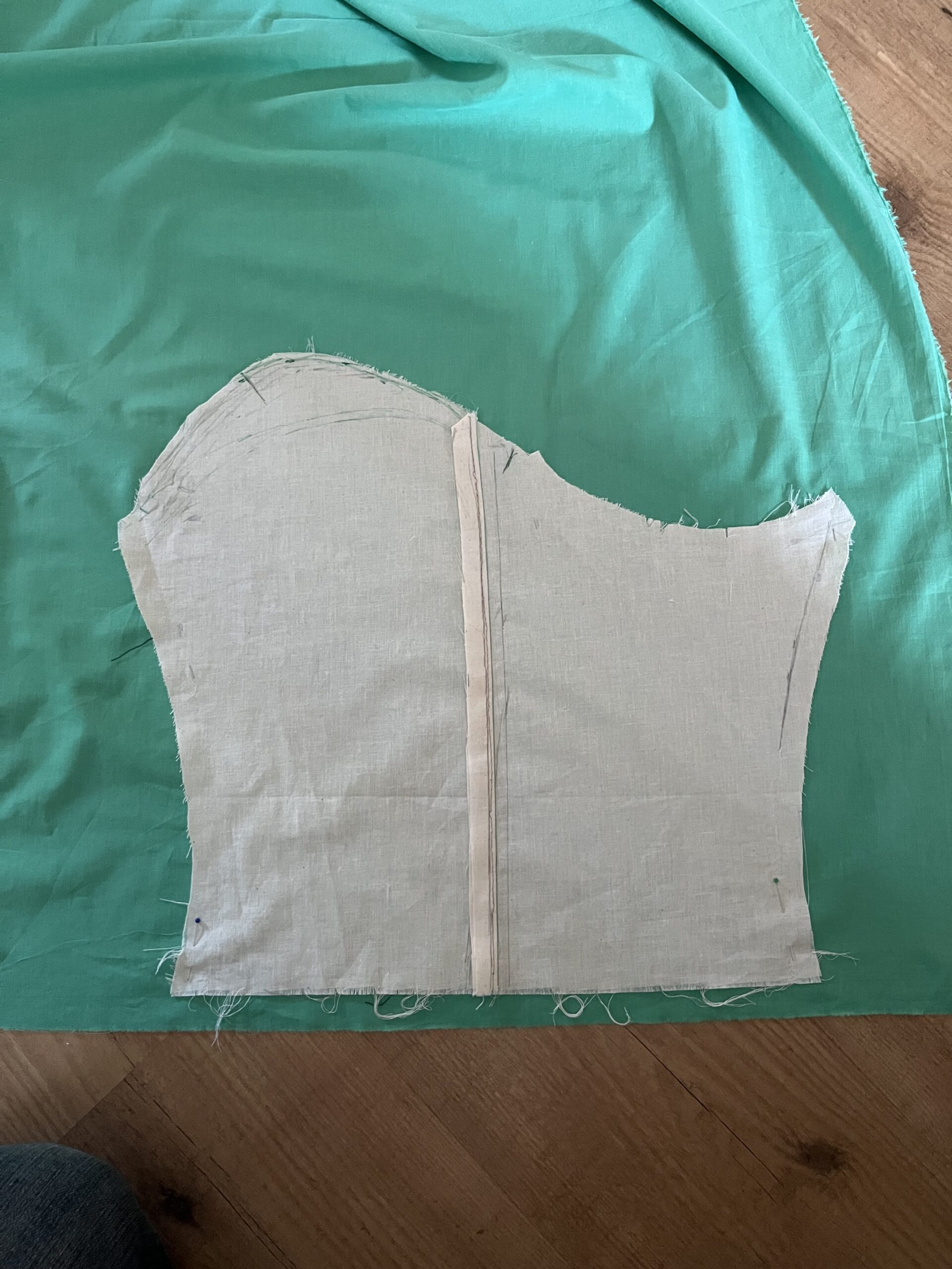 A muslin sleeve shape is laid out on a piece of green fabric.