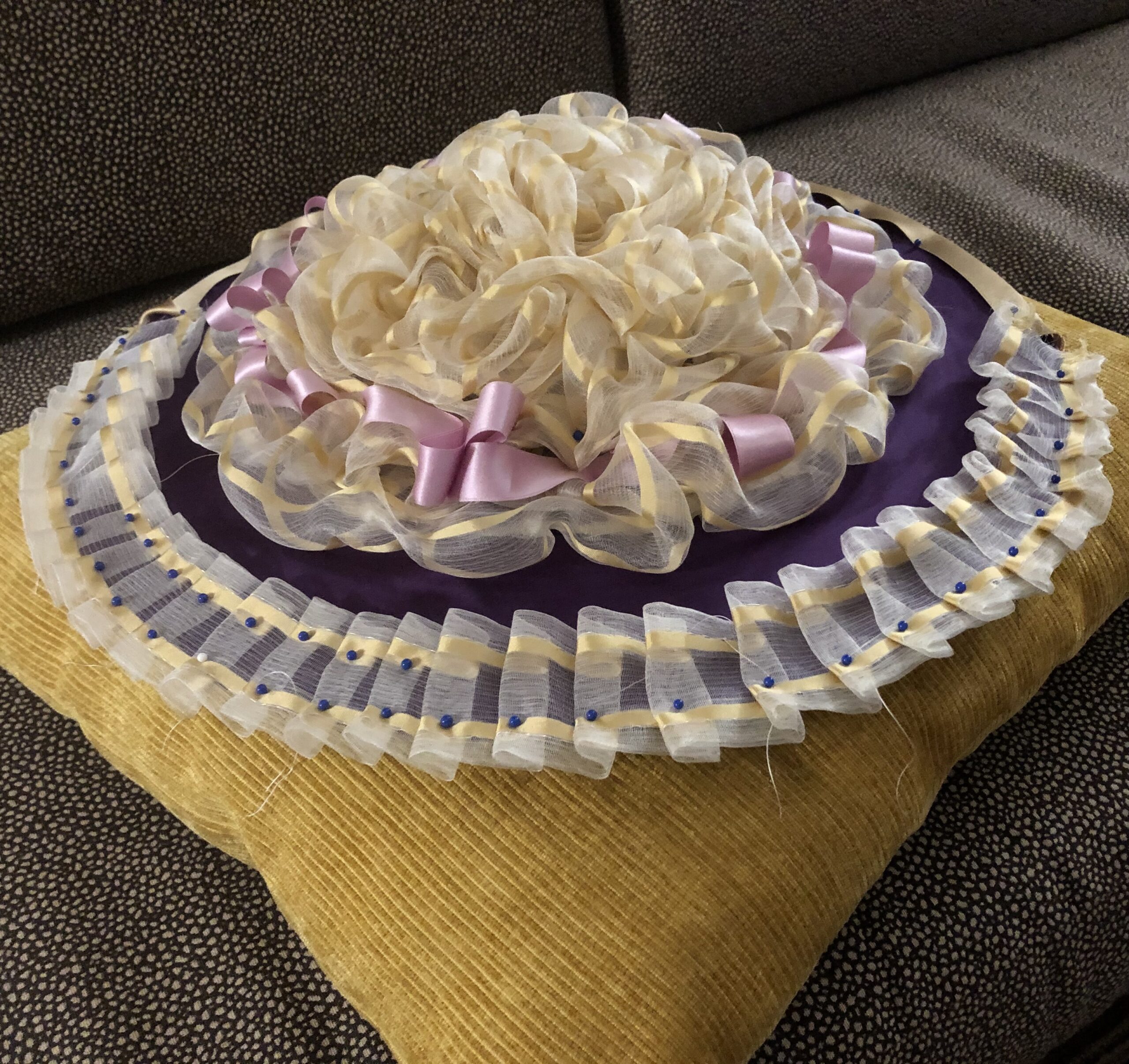 A trimmed 18th Century bergere hat sits on a sofa cushion.