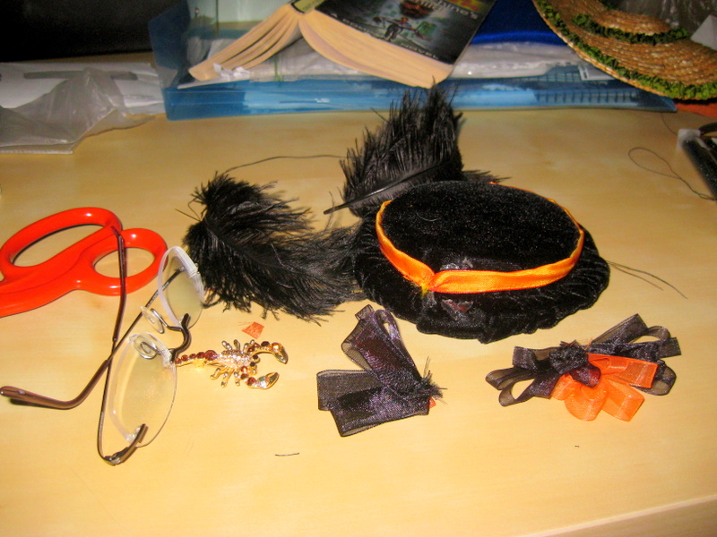 A black 1860s doll hat lies on the floor in a pile of ribbons and trims 