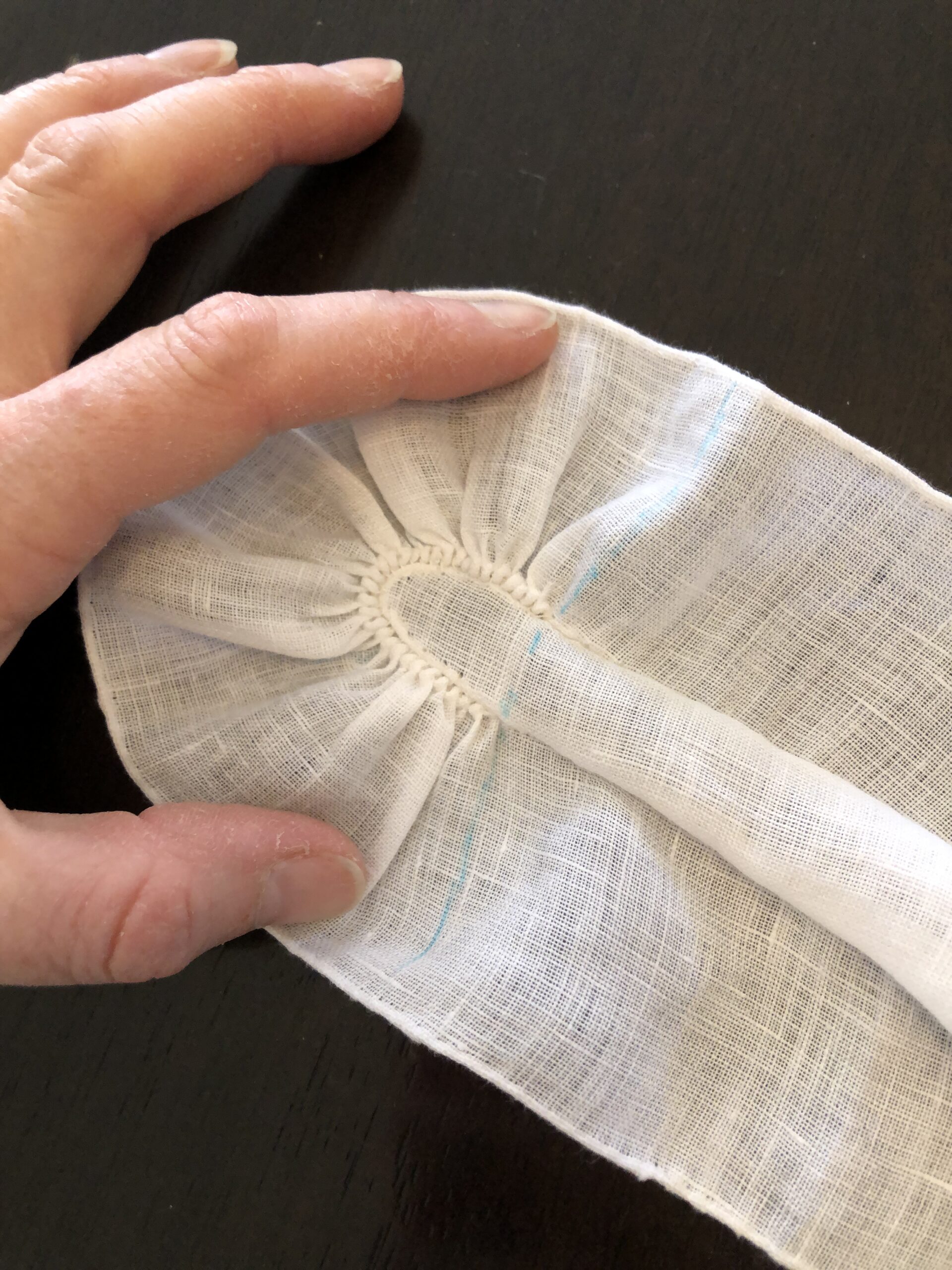 A hand spreads out a tightly gathered ruffle that wraps around a point of fabric.