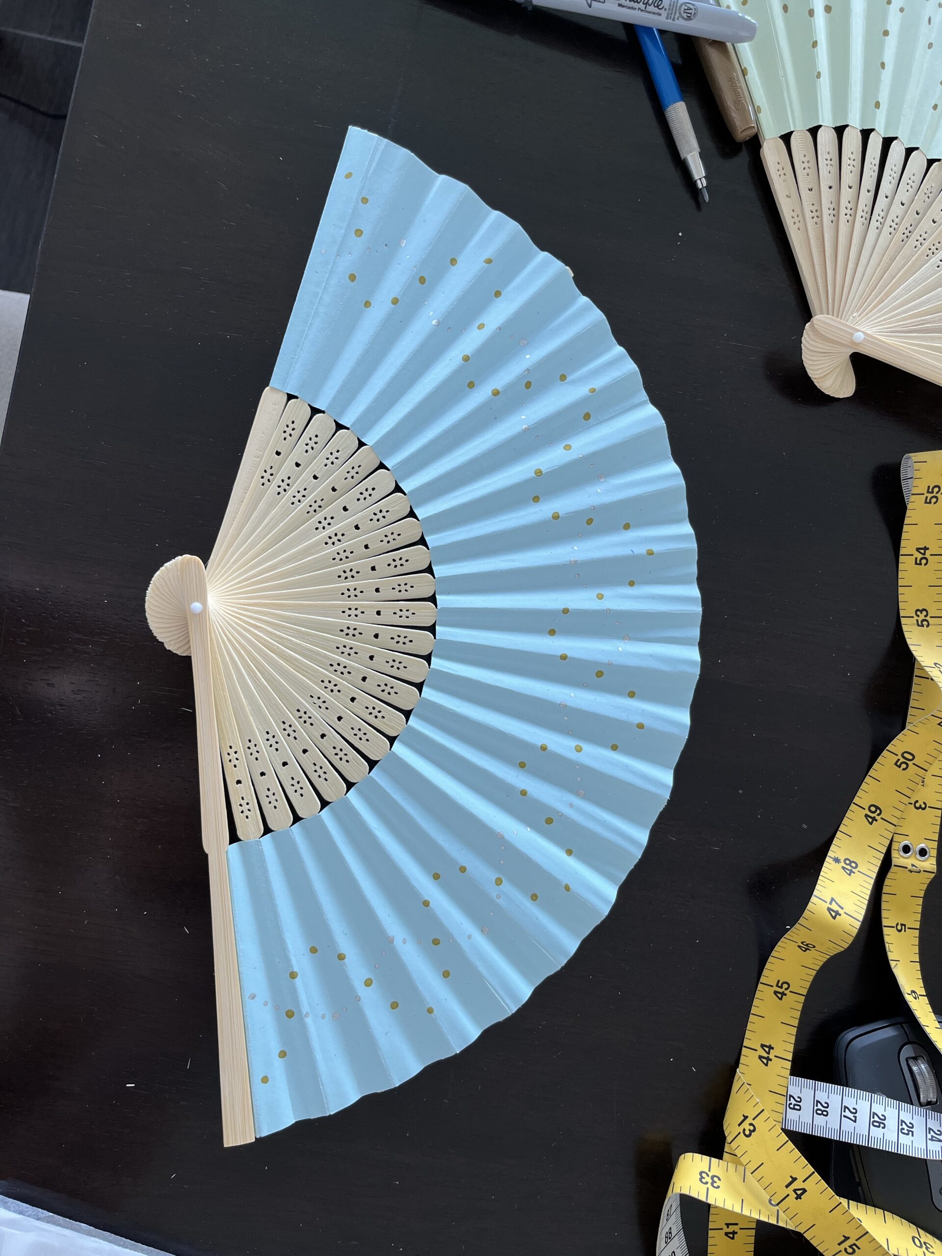 a blue paper fan, painted in wave patterns of gold and silver polka dots