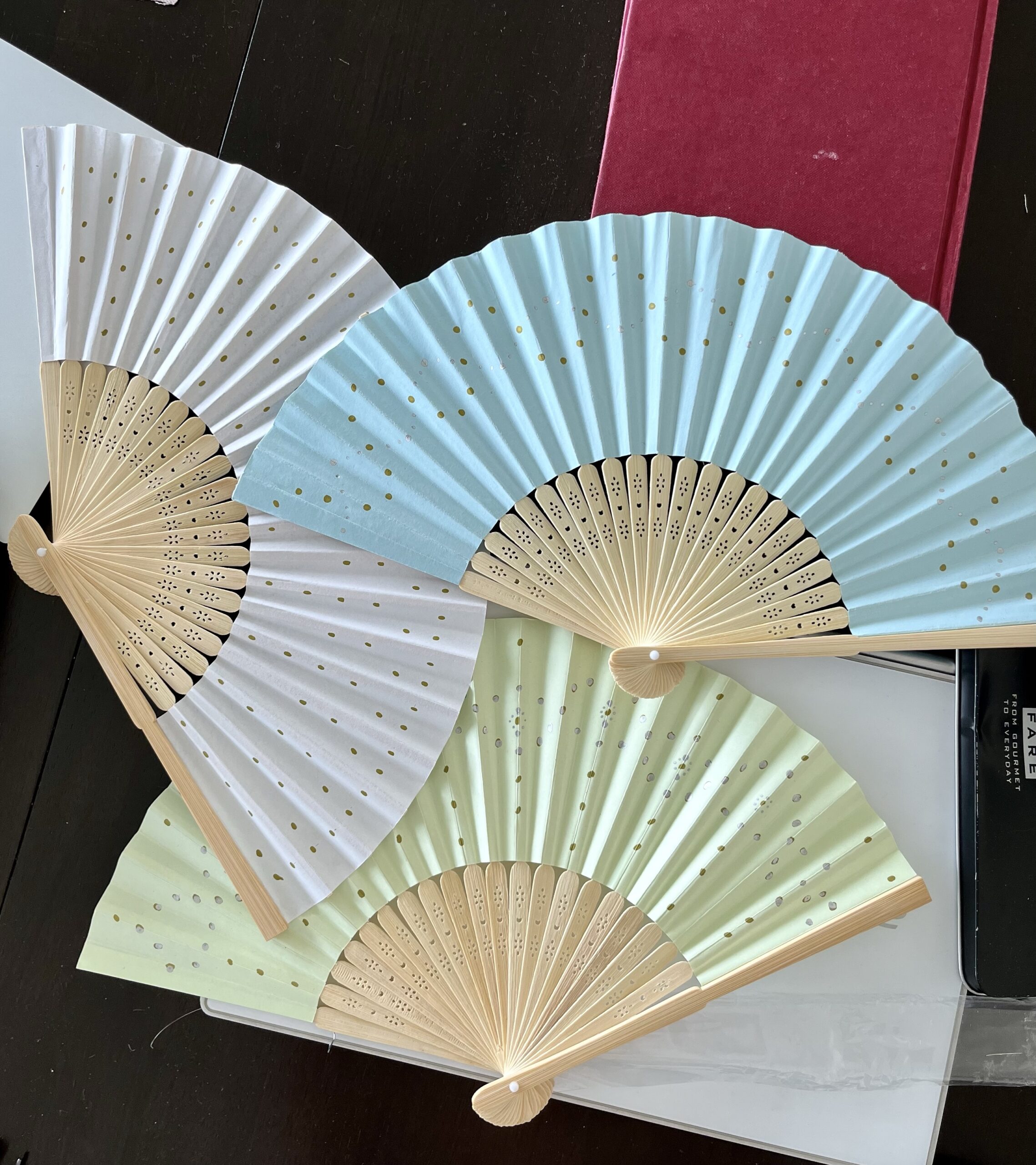Three paper fans, white blue and green, painted in varying dot patterns with gold and silver pens.