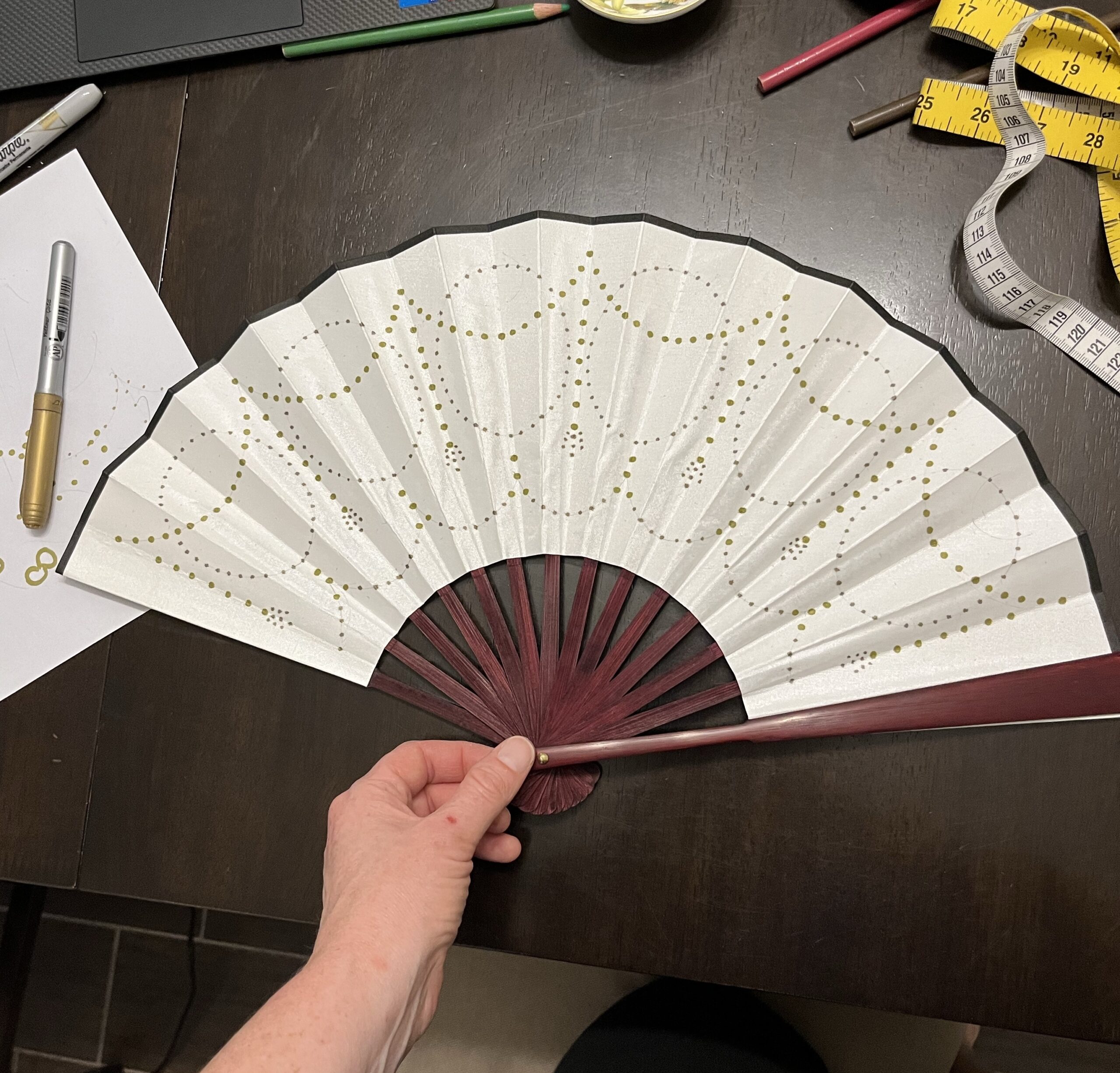 A white paper fan painted with arabesques of gold polka dots.