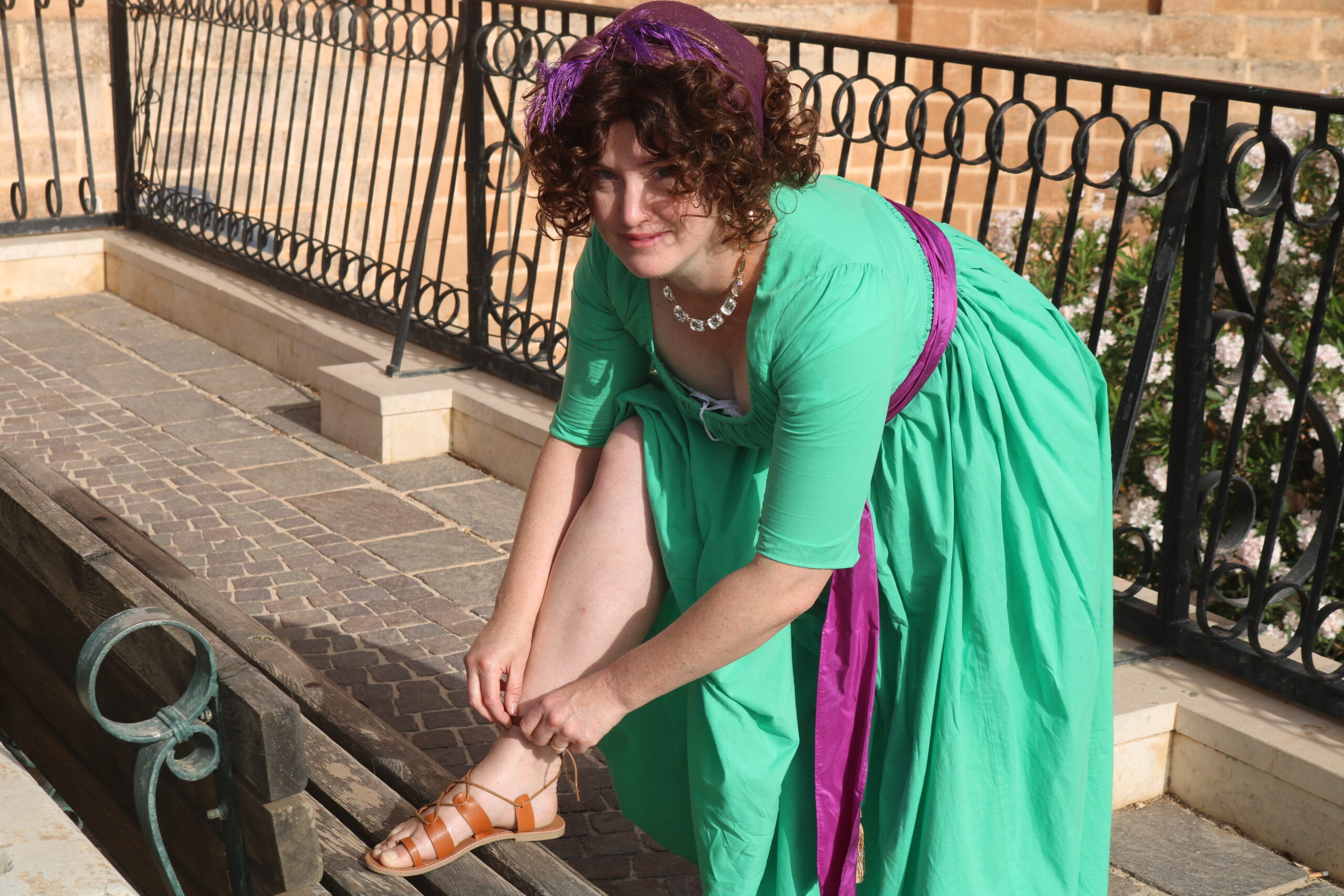 Tabubilgirl wearing a 1790s round gown bends to tie her sandal