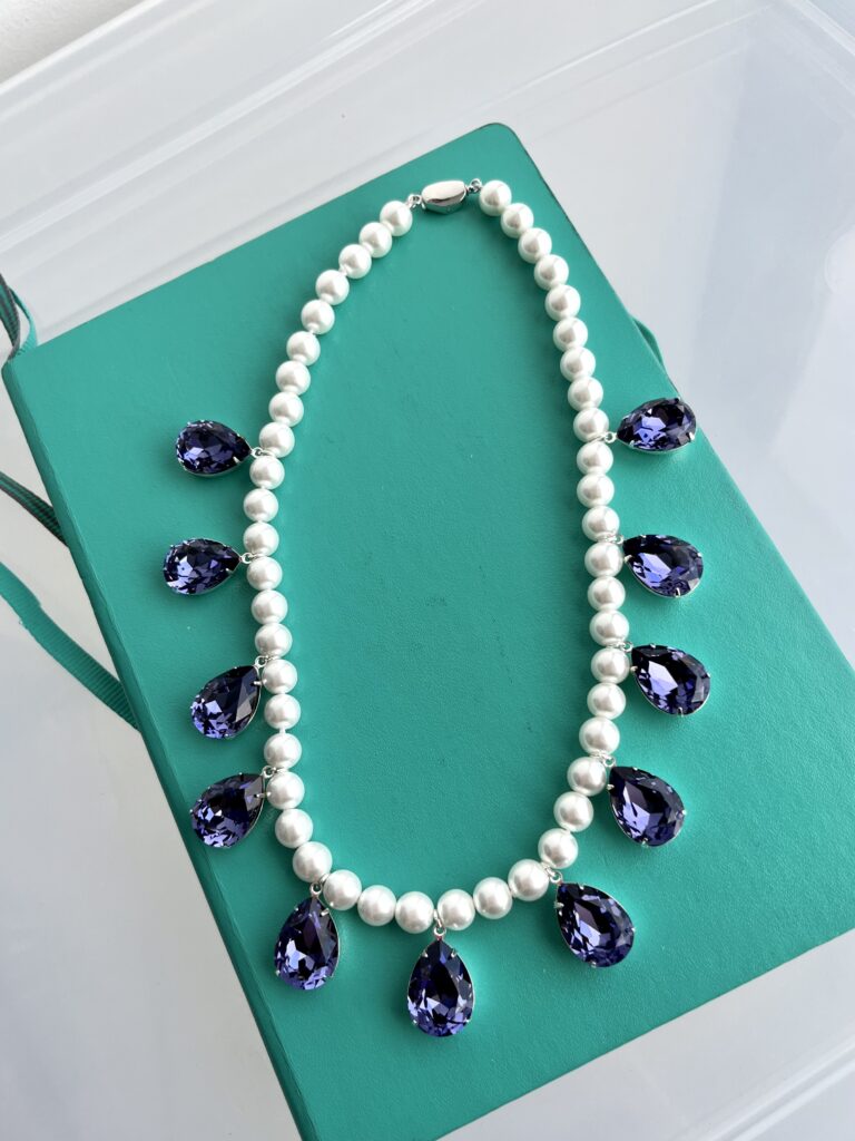 A pearl necklace with pendant purple pear-shaped drops sits on a green book.