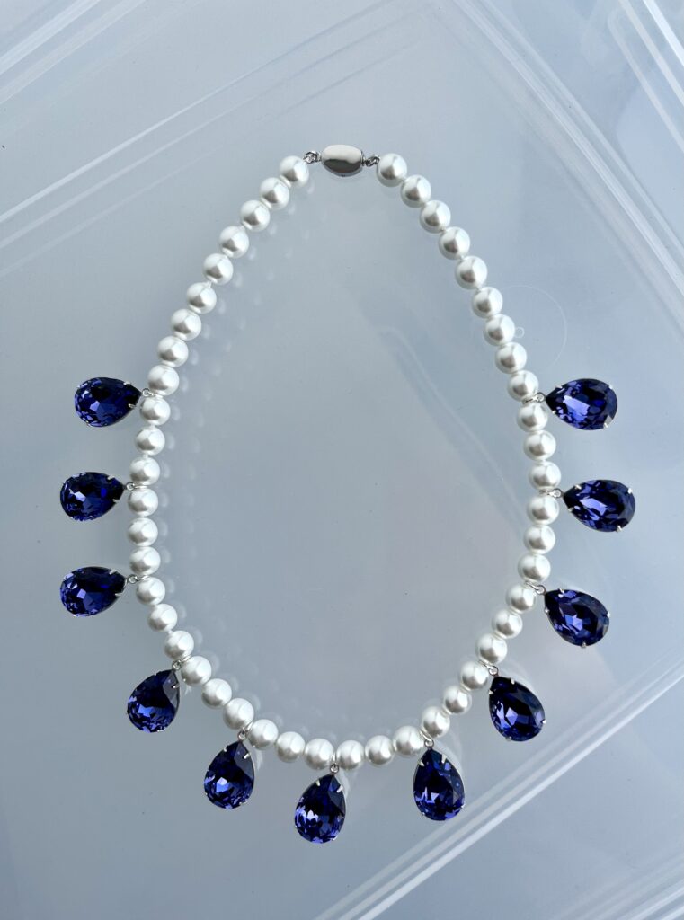 A pearl necklace with pendant purple crystal drops lies on a clear plastic background